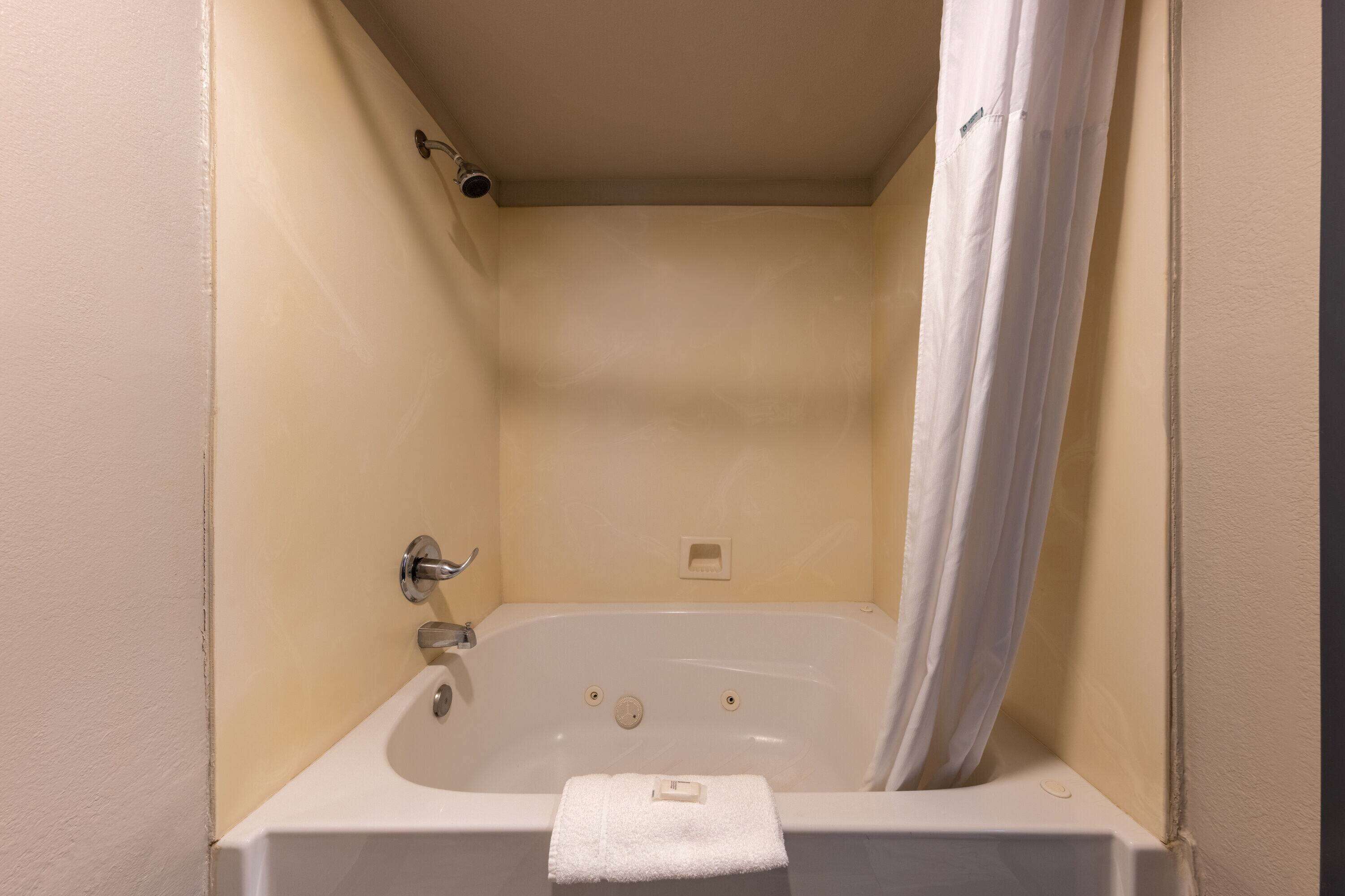 A small, white bathtub with a shower curtain, a towel, and a faucet.