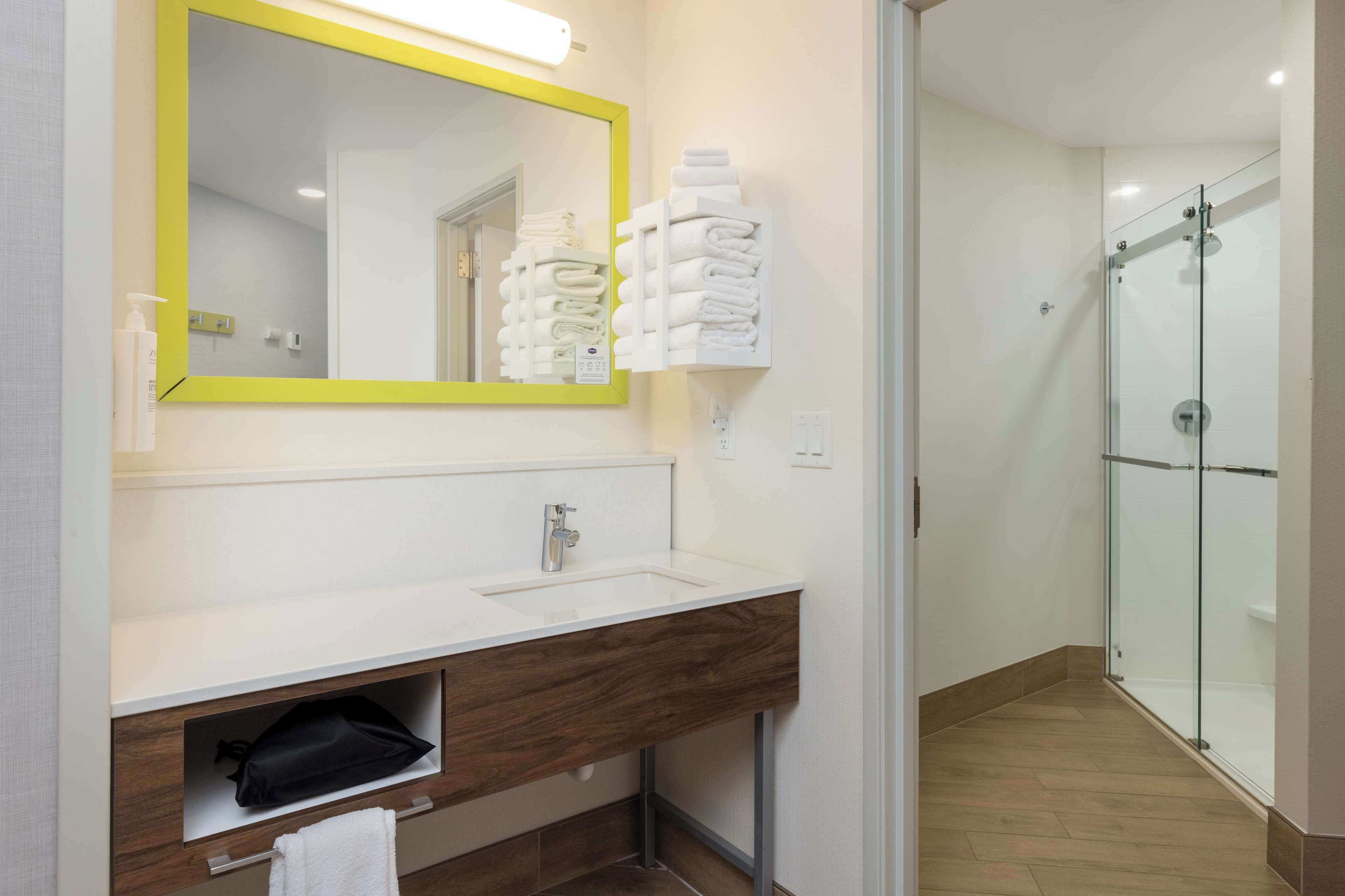 Une salle de bain moderne avec un lavabo blanc, un miroir à cadre jaune et une cabine de douche en verre.