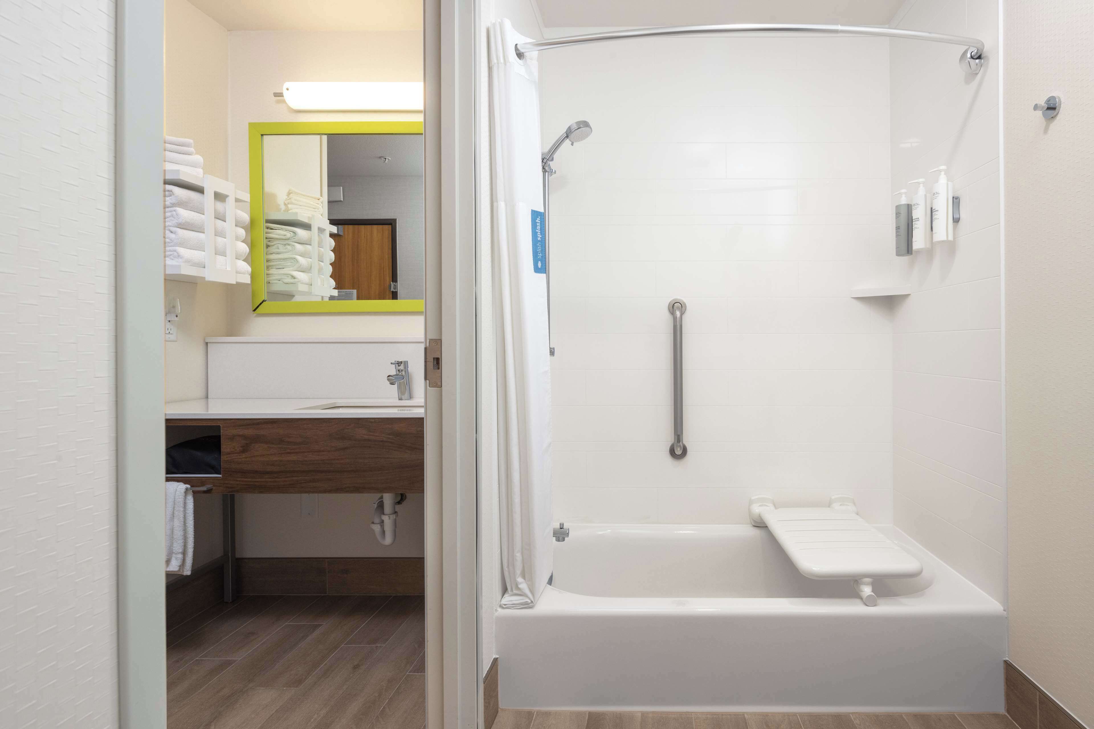A modern bathroom with a walk-in shower, a toilet with a grab bar, and a sink area with a mirror and towel rack.