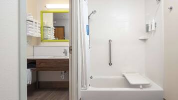 A modern bathroom with a walk-in shower, a toilet with a grab bar, and a sink area with a mirror and towel rack.