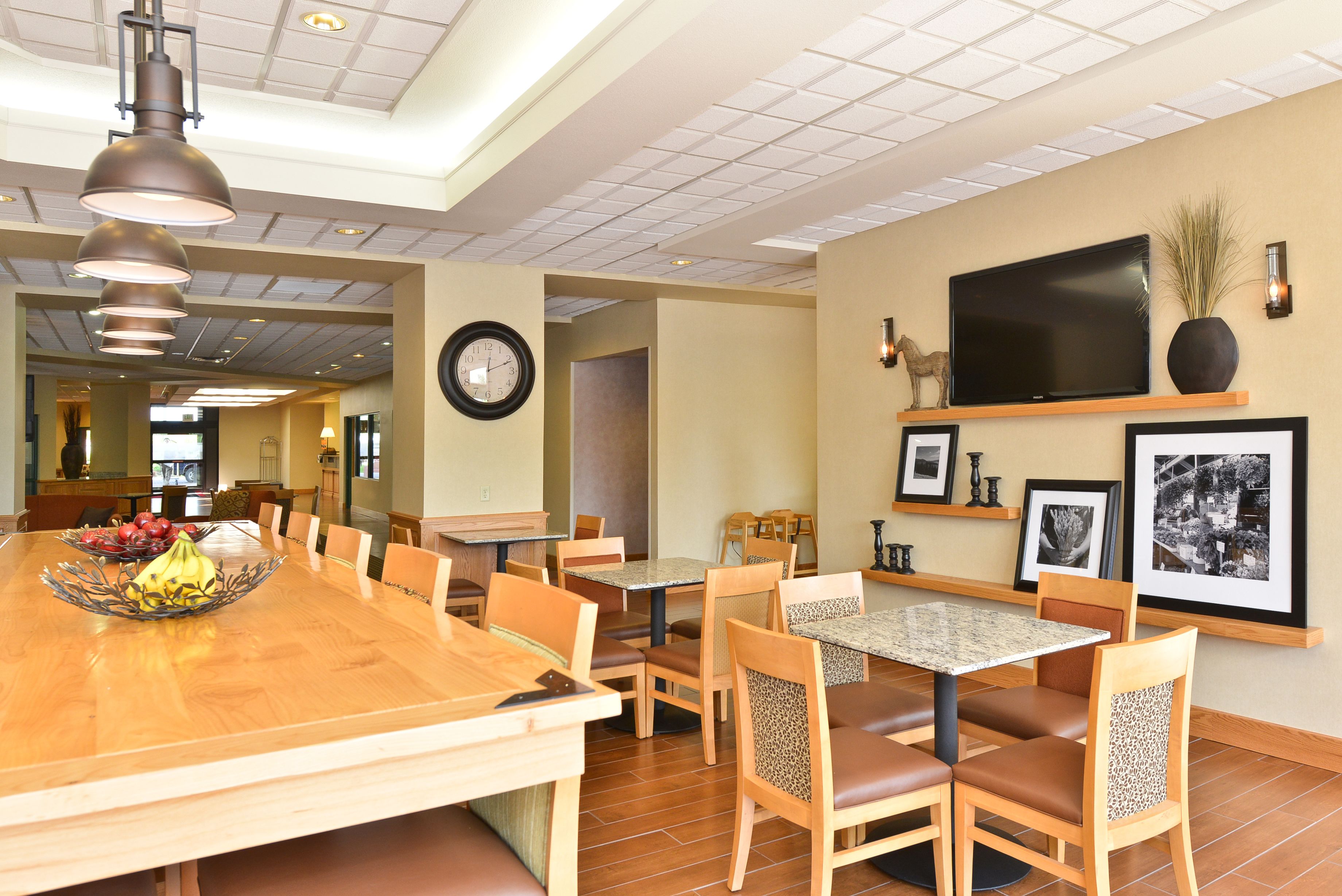 Un restaurante con una amplia mesa de comedor de madera, múltiples sillas, un televisor montado en la pared y cuadros enmarcados.