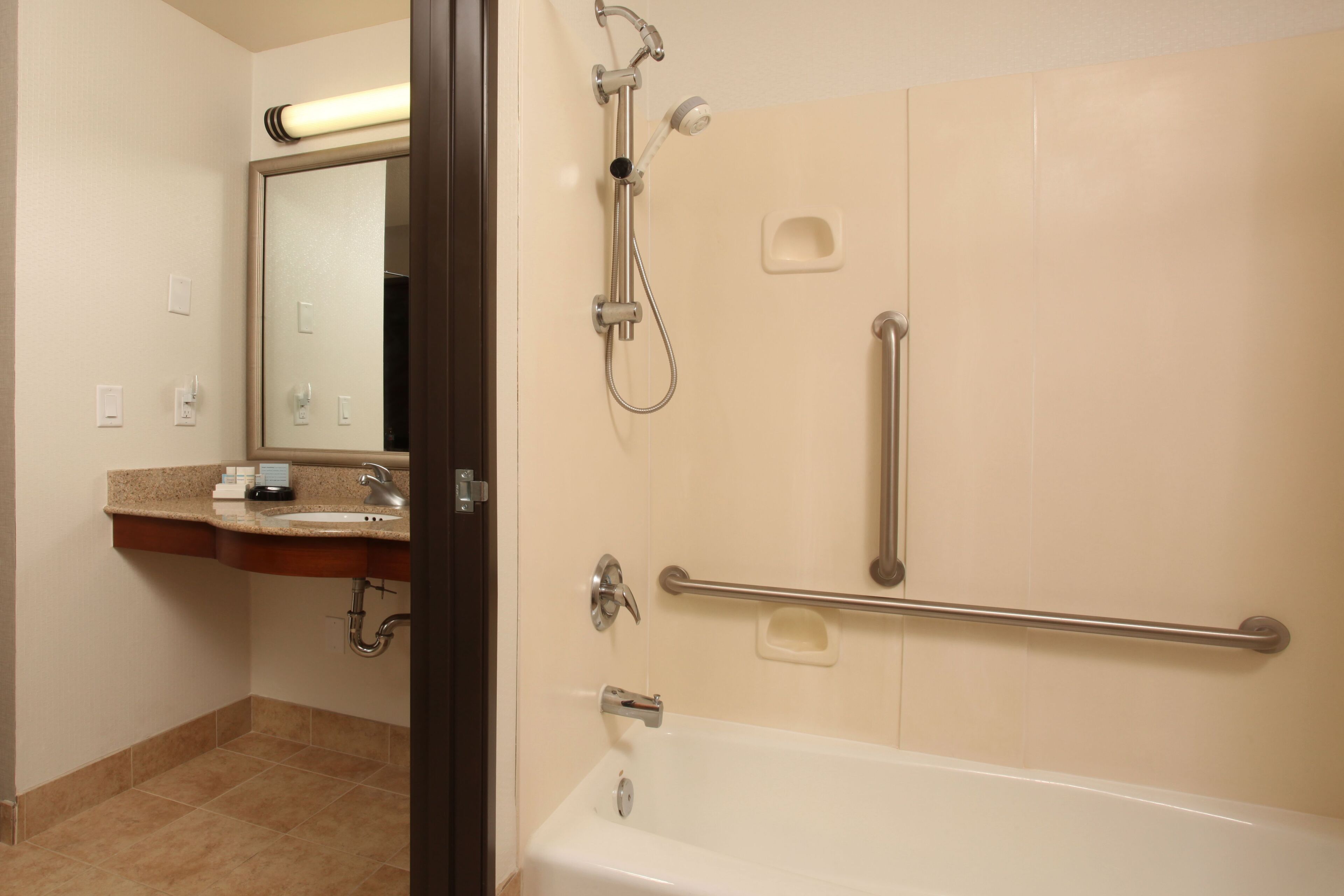 A bathroom with a bathtub, a shower, a vanity with a mirror, and a handrail.