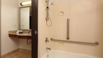 A bathroom with a bathtub, a shower, a vanity with a mirror, and a handrail.