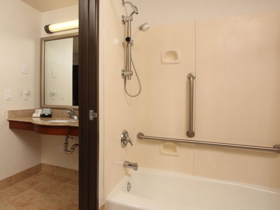 A bathroom with a bathtub, a shower, a vanity with a mirror, and a handrail.