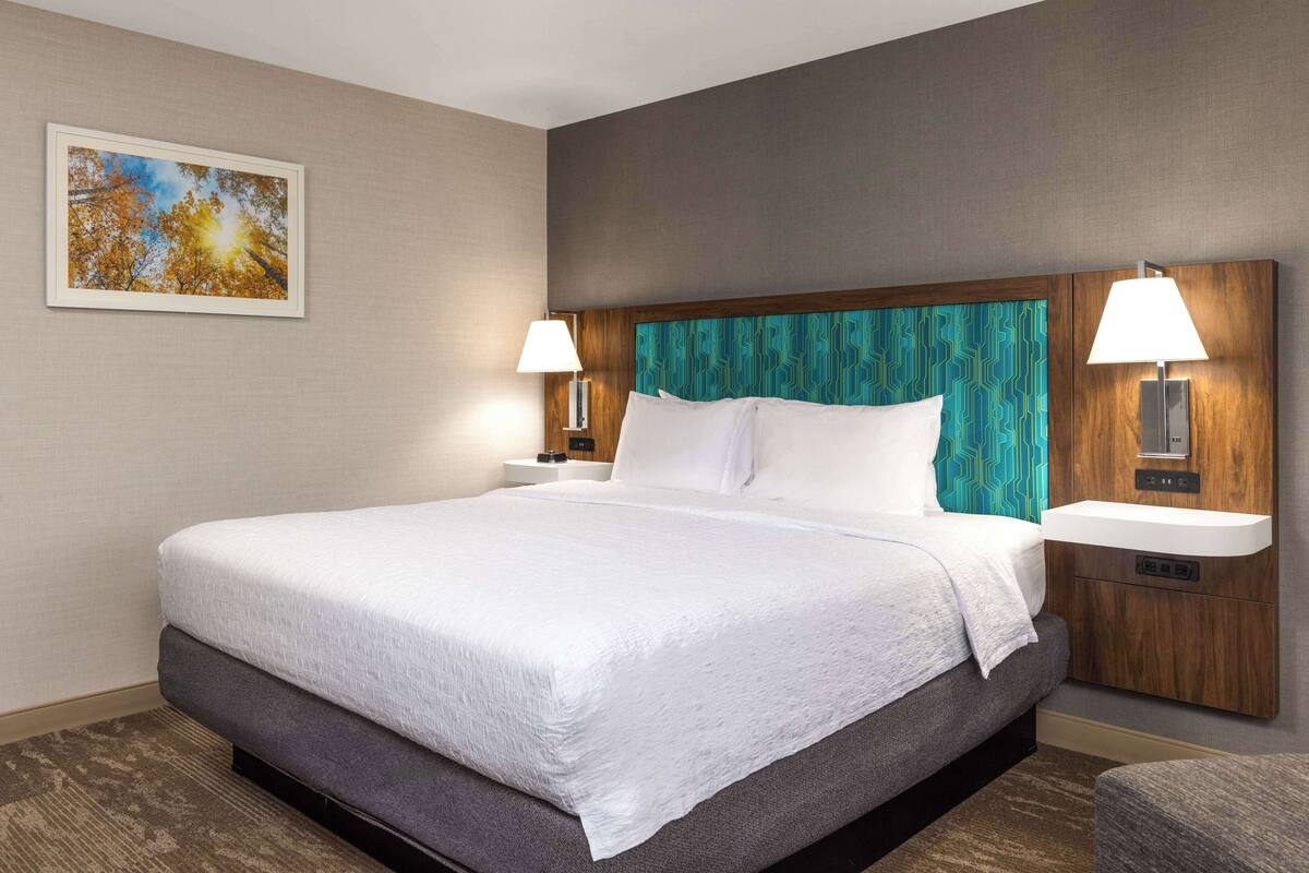 A hotel room with a large bed, two bedside tables with lamps, a wall-mounted TV, and a framed picture on the wall.