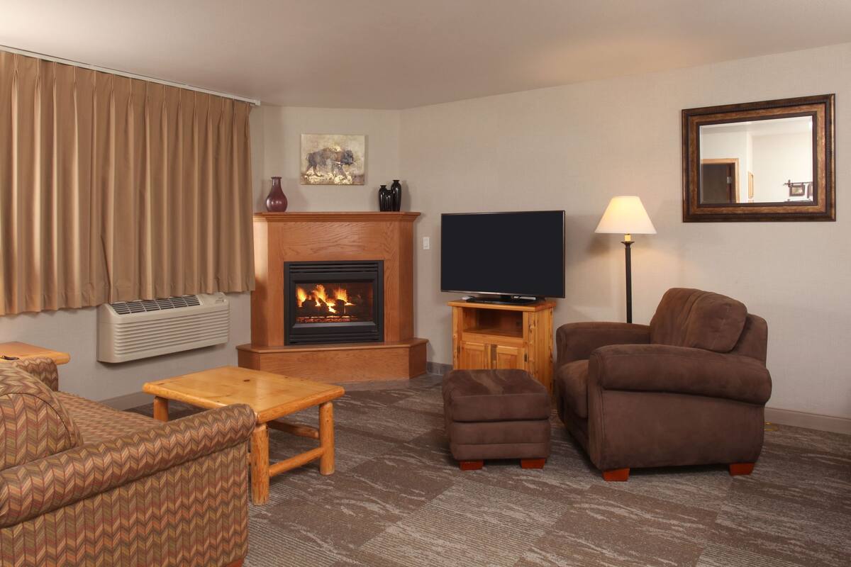 A living room with a fireplace, a television, a sofa, an ottoman, and a lamp.