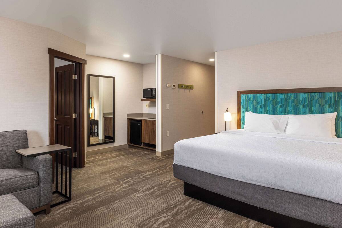 A hotel room with a bed, a seating area, a desk, and a mirror.
