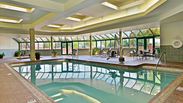 An indoor swimming pool with clear glass walls, a tiled floor, and a sunlit ceiling. - Hampton Inn Kalispell (Kalispell)