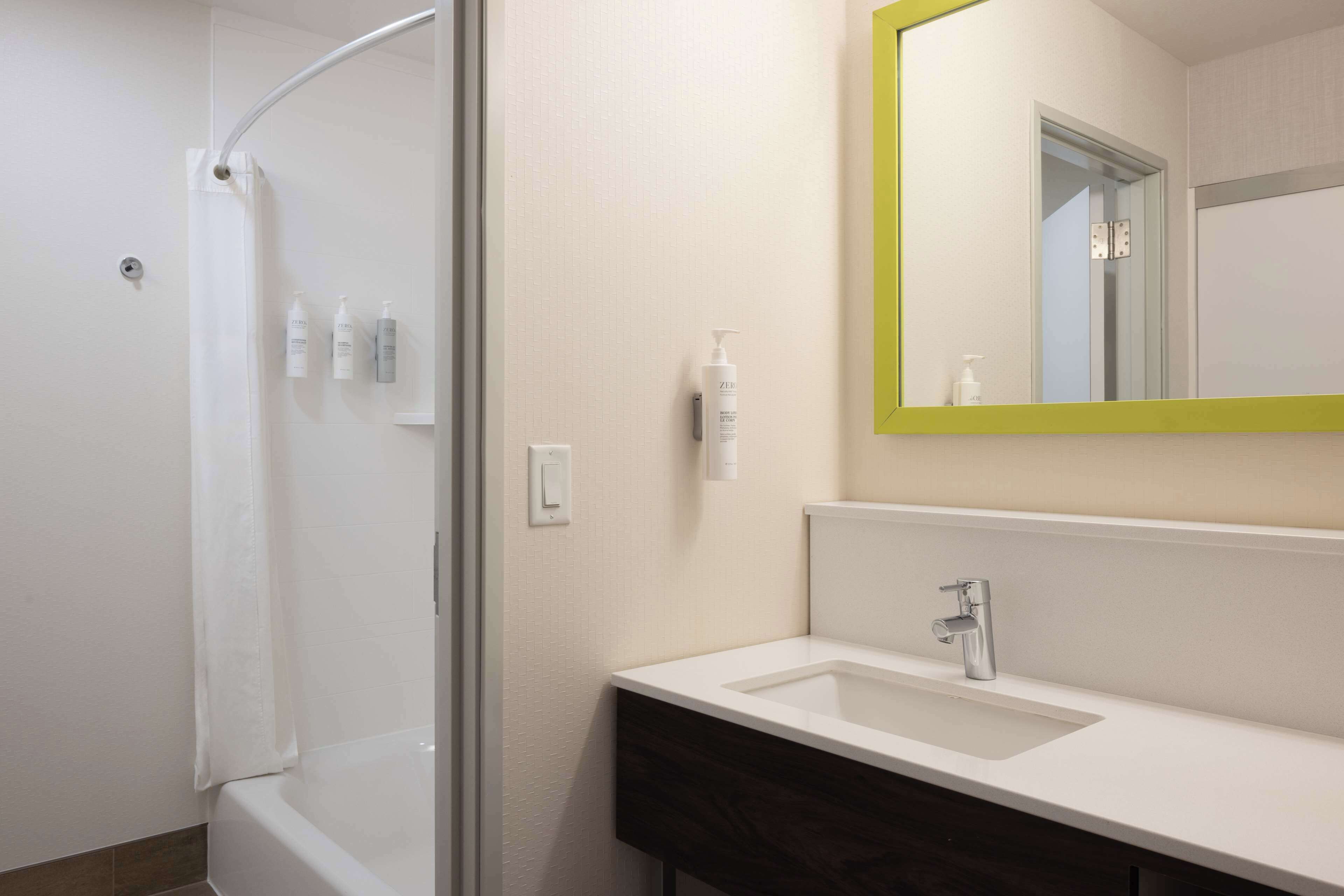 A modern bathroom with a shower, a sink, and a mirror with a green frame.