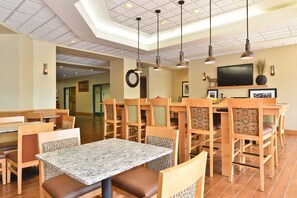 A restaurant with wooden tables and chairs, a television mounted on the wall, and a clock on the wall.