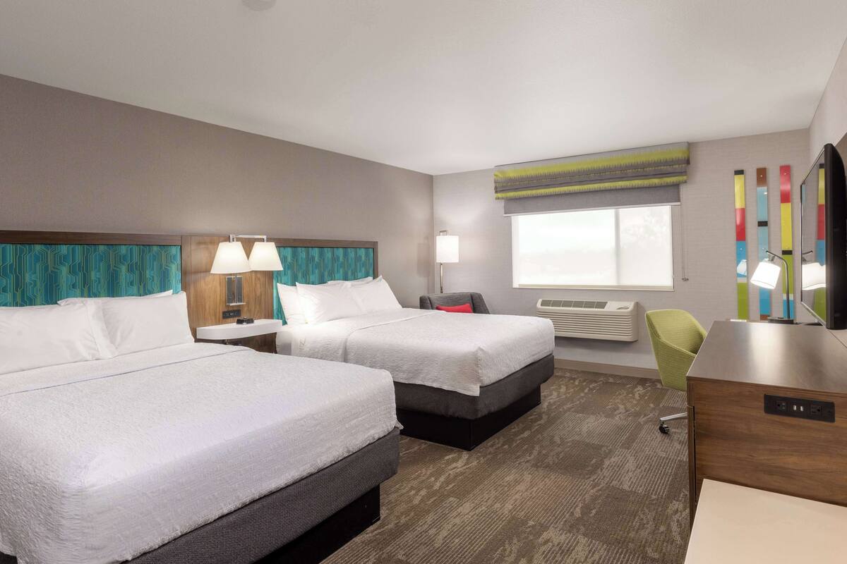 A hotel room with two beds, a desk, a chair, a TV, and a window with a view.