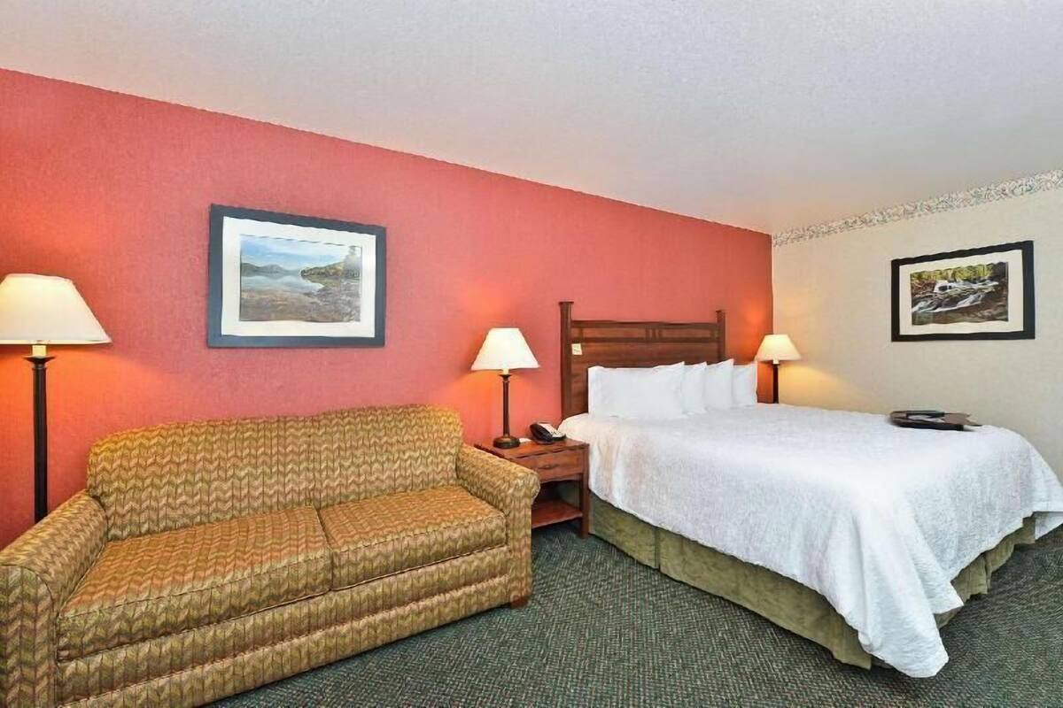 A hotel room with a bed, a sofa, two lamps, and two framed pictures on the walls.