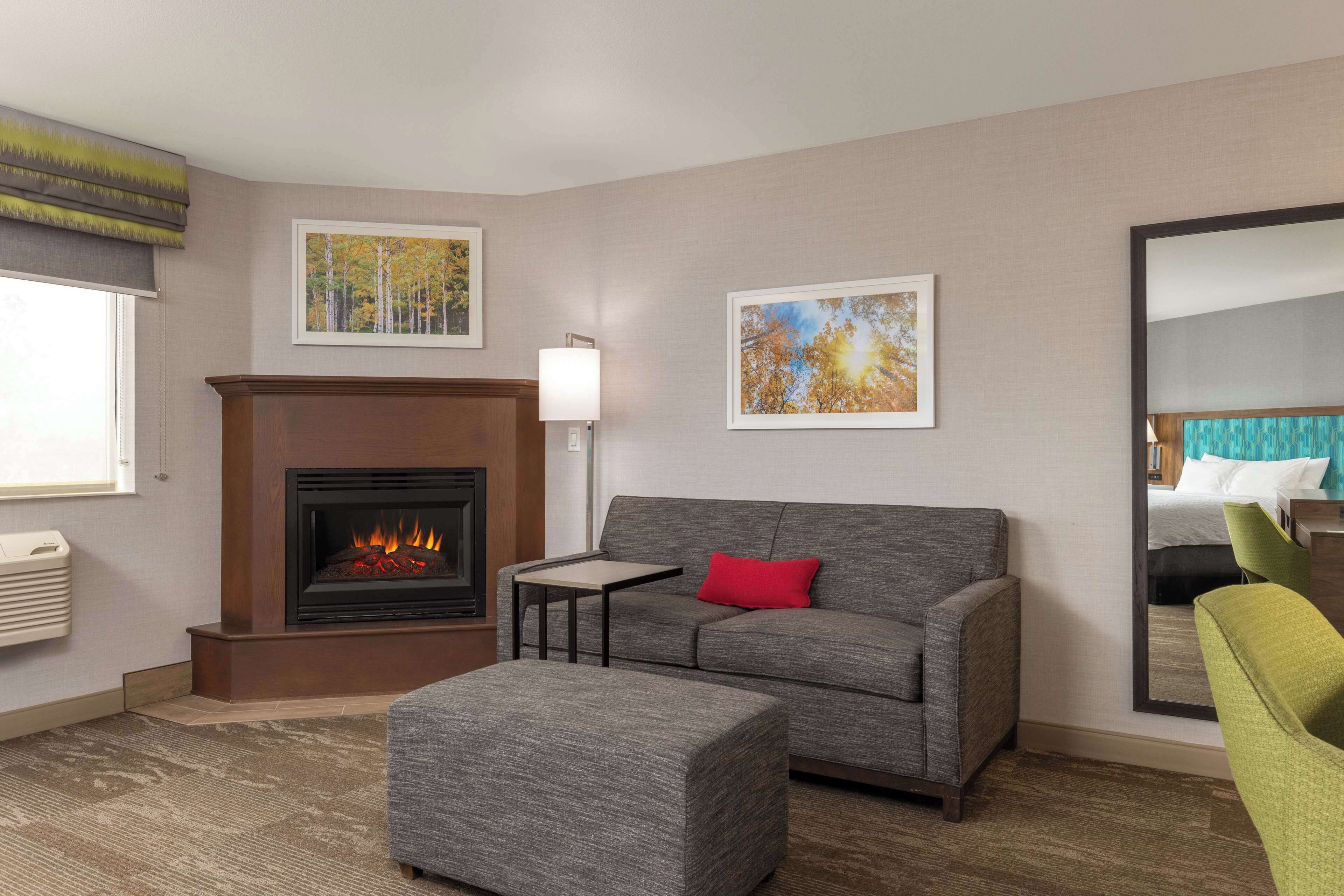 A modern living room with a fireplace, grey sofa, ottoman, and a green armchair.