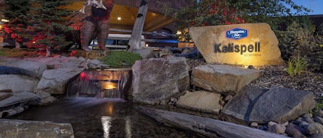 A hotel sign with a bear sculpture and a small waterfall.