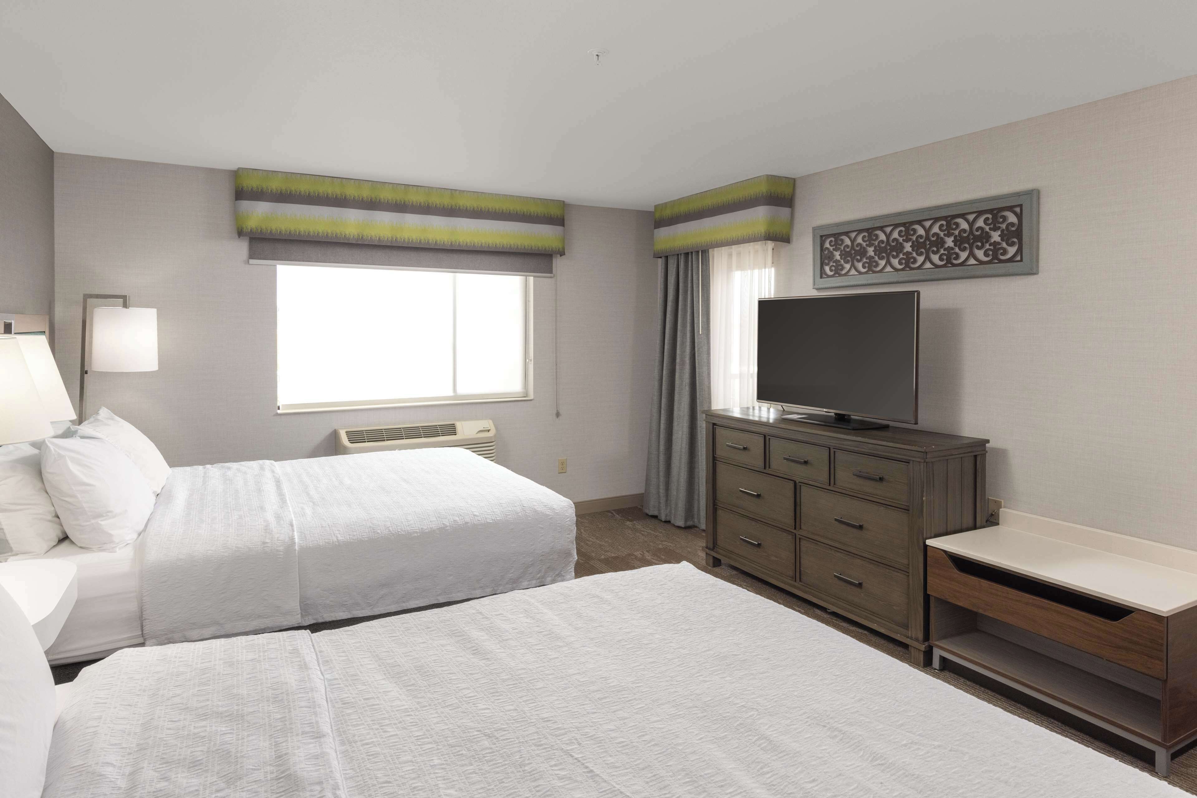 Habitación de hotel con dos camas, televisión, cómoda y ventana con cortinas.