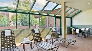 A sunlit indoor patio with metal loungers, a small table, and a view of greenery outside. - Hampton Inn Kalispell (Kalispell)