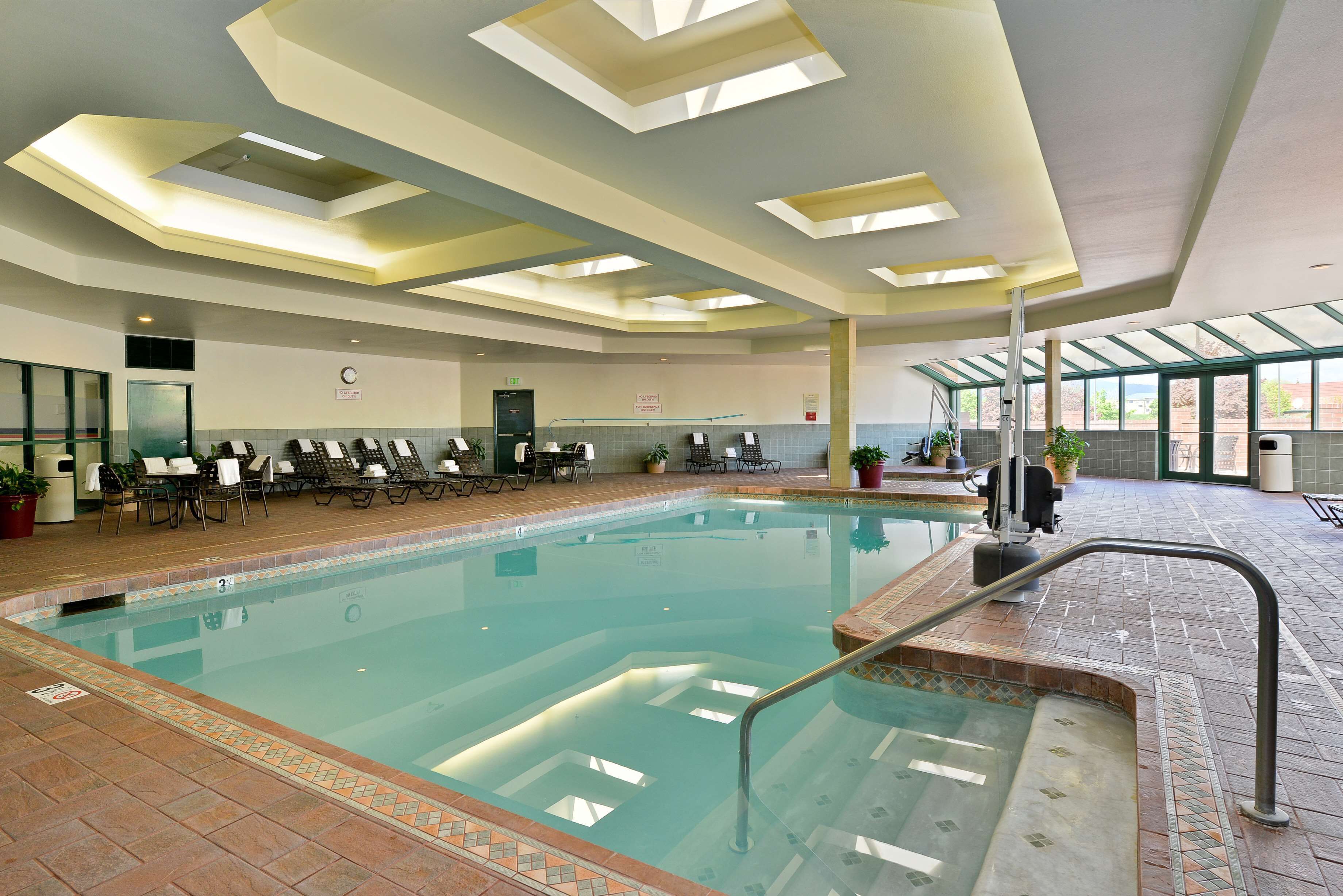 An indoor swimming pool with clear water, a tiled deck, and a seating area with chairs and tables.