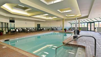 An indoor swimming pool with clear water, a tiled deck, and a seating area with chairs and tables.