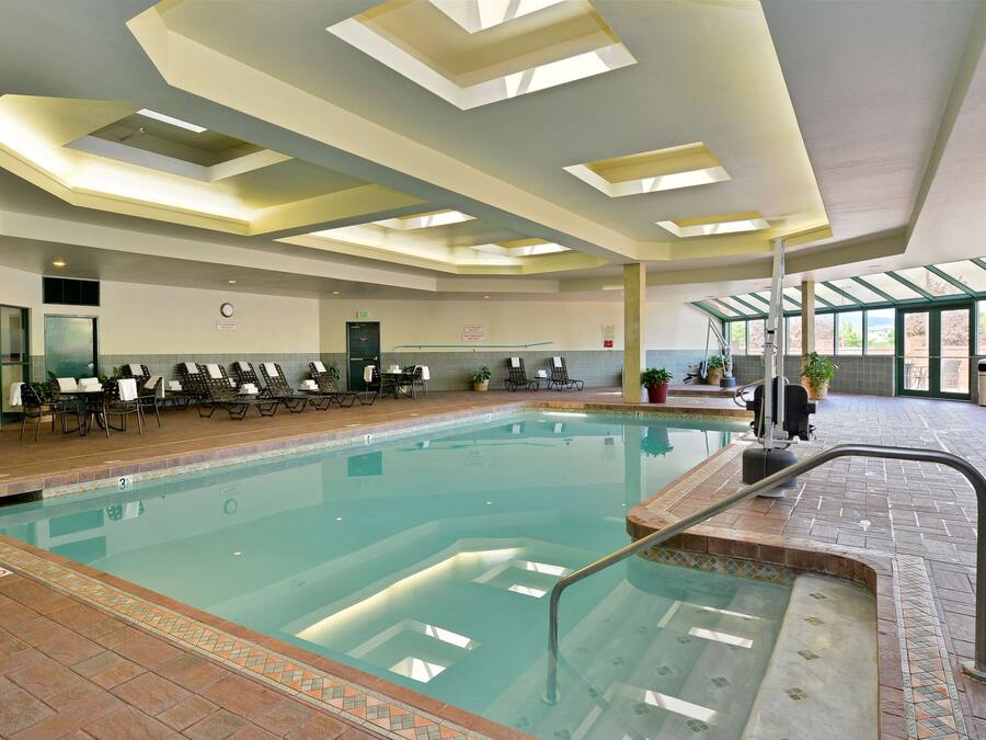 An indoor swimming pool with clear water, a tiled deck, and a seating area with chairs and tables.