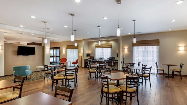 A hotel dining area with multiple tables and chairs, a television mounted on the wall, and a reception desk in the background. - Sleep Inn & Suites Miles City I-94 (Miles City)