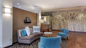 A modern lobby with a sofa, blue armchairs, a patterned rug, and a wall with a nature-inspired mural. - Sleep Inn & Suites Miles City I-94 (Miles City)