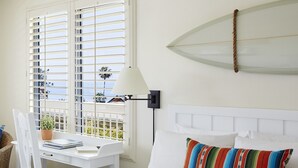 A hotel room with a bed, a desk with a chair, a lamp, and a surfboard on the wall. - Laguna Beach House (Laguna Beach)