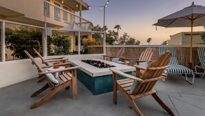 An outdoor patio with wooden chairs, a fire pit, and string lights. - Laguna Beach House (Laguna Beach)