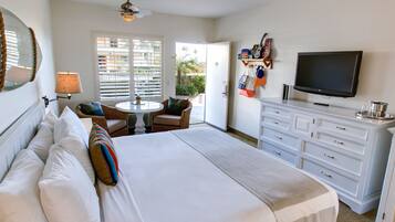 A hotel room with a large bed, a TV, a dresser, a chair, a table, and a balcony with a view of the outside.