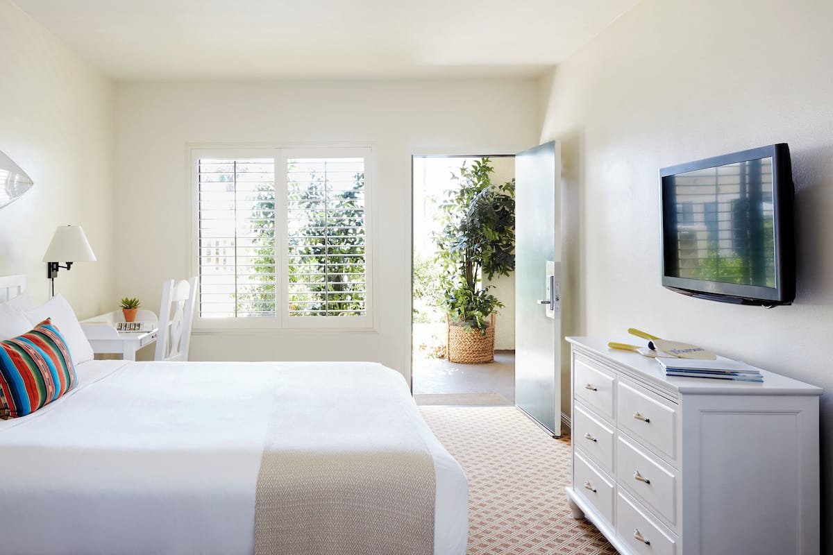 Quarto de hotel com uma cama, televisão, escrivaninha e janela com persianas.