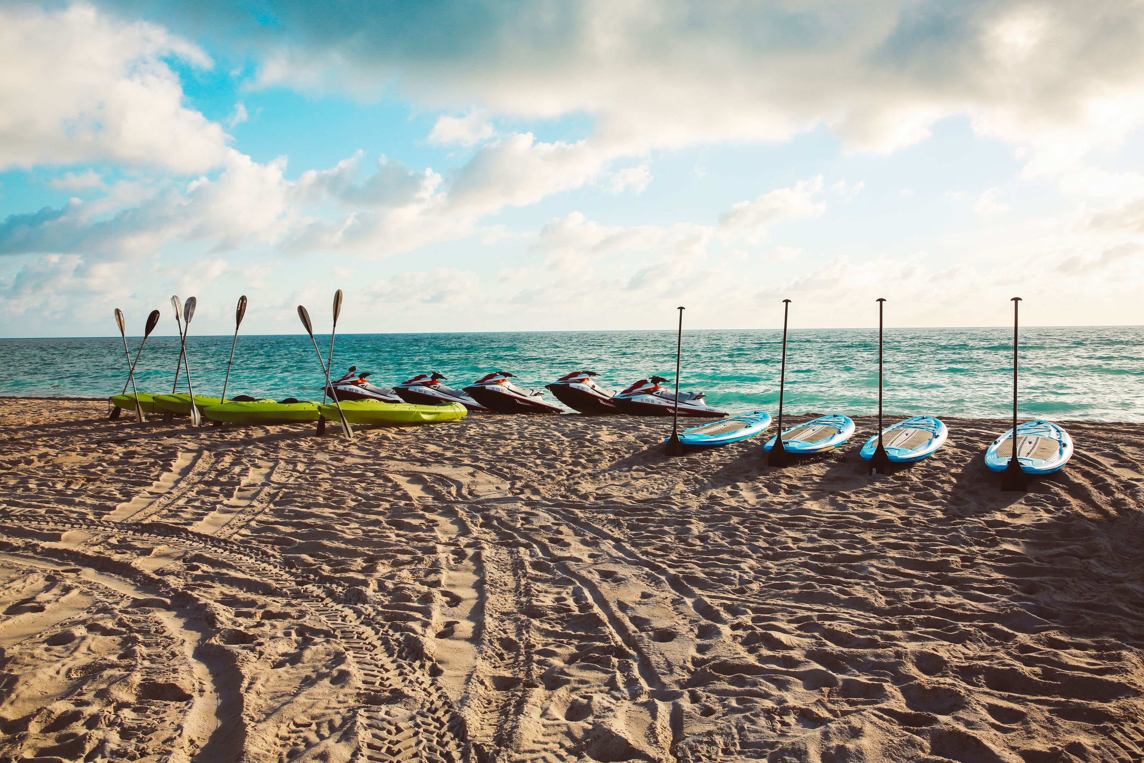 A beach with kayaks lined up on the sand, a clear sky, and the ocean in the background.