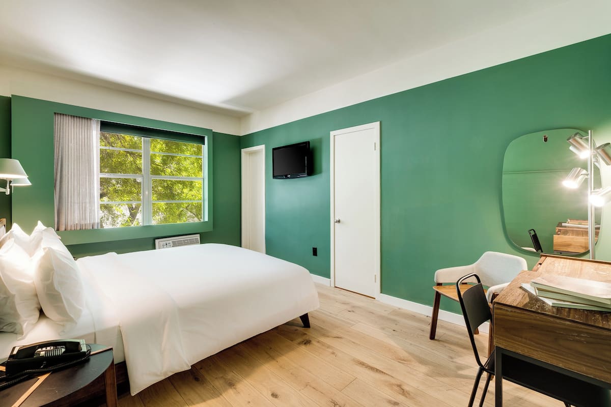 A room with a bed, a desk, a chair, a TV, and a window with curtains.