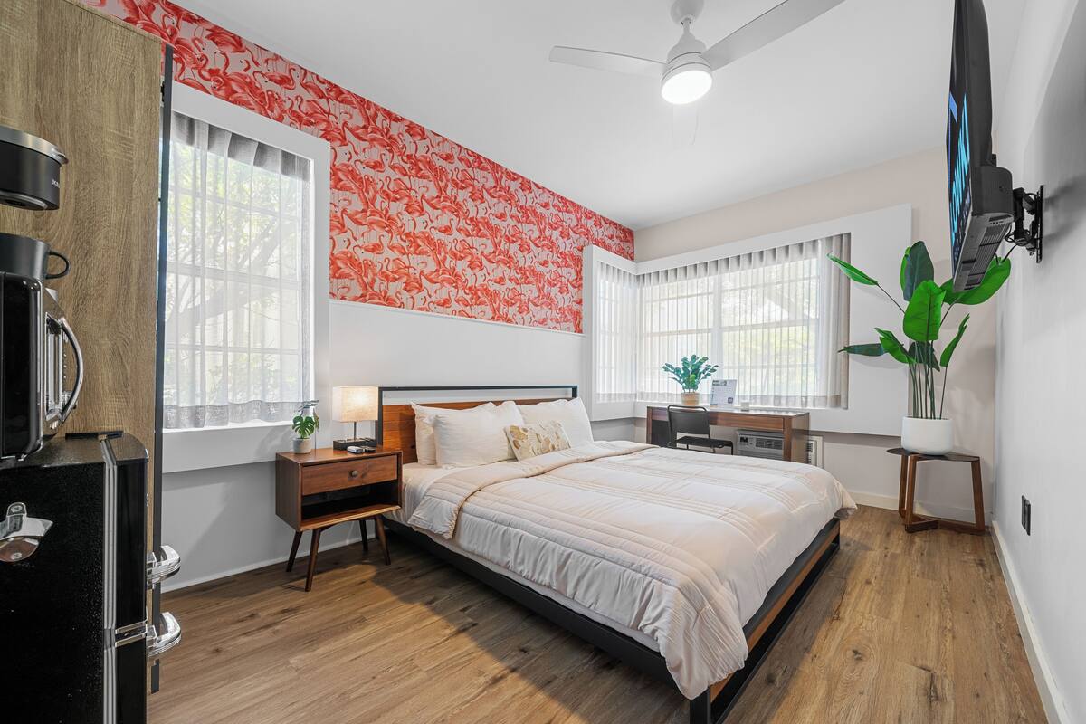 A bedroom with a bed, nightstands, a desk, and a potted plant.