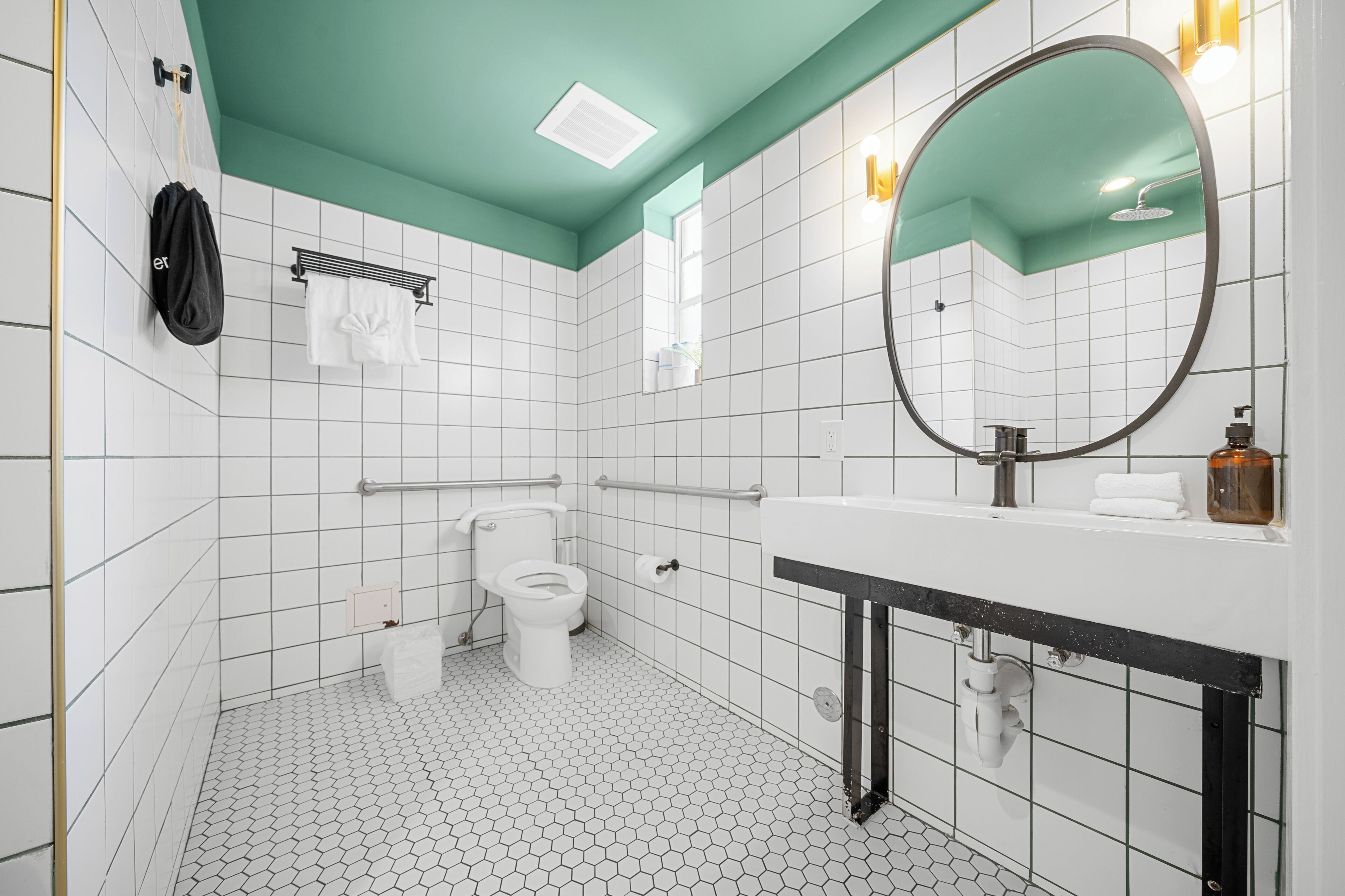 Ein modernes Badezimmer mit weißen, sechseckigen Fliesen, einer weißen Toilette, einem Waschbecken mit schwarzer Arbeitsplatte, einem Spiegel und einem Handtuchhalter.