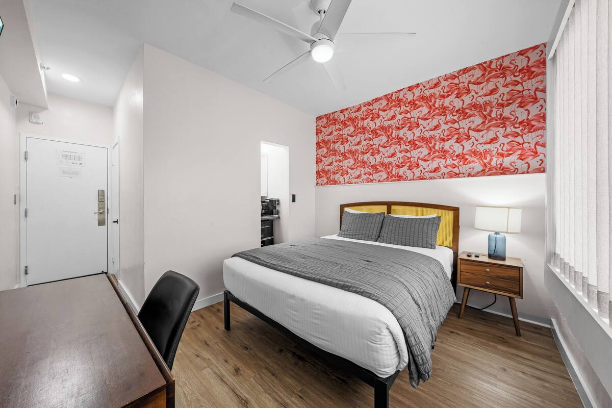 A hotel room with a bed, a desk, a chair, a nightstand, a lamp, and a ceiling fan.