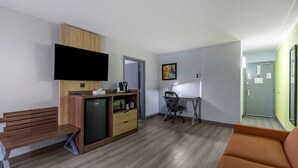 A compact living space with a kitchenette, a flat-screen TV, a desk with a chair, a bench, and a sofa.