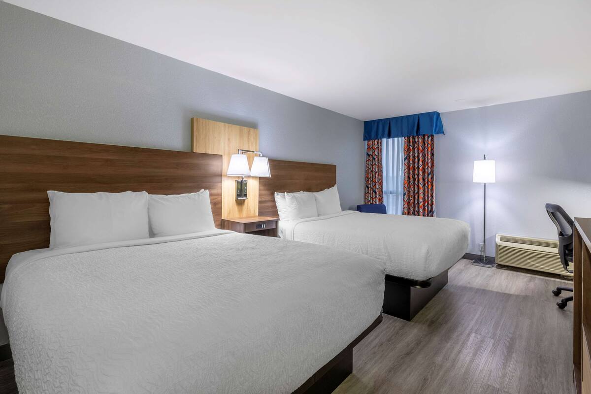 Een hotelkamer met twee bedden, een bureau, een stoel, een lamp en een raam met gordijnen.