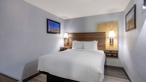 A hotel room with a large bed, two bedside tables with lamps, a wooden headboard, and a framed picture on the wall.