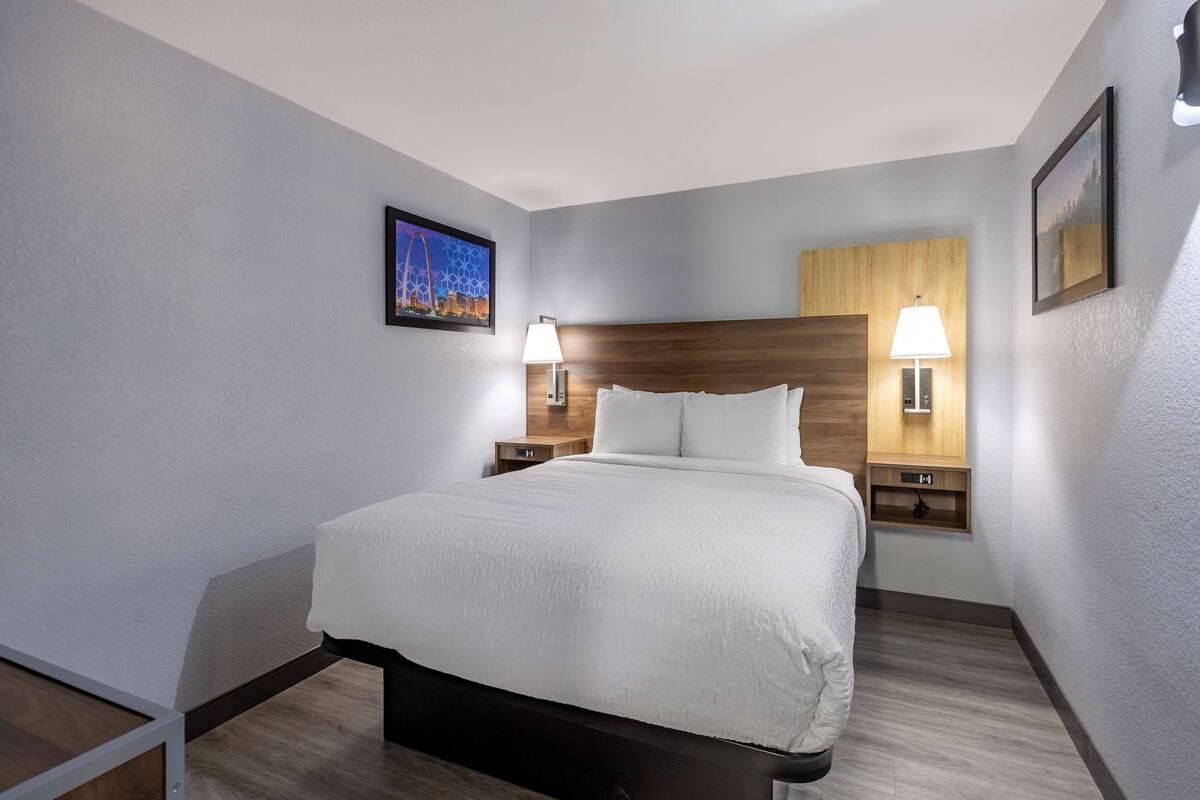 Een hotelkamer met een groot bed, twee nachtkastjes met lampen, een houten hoofdbord en een lijst met een afbeelding aan de muur.