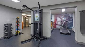 Een sportschool met een loopband, krachttoestellen en een dumbbellsysteem.