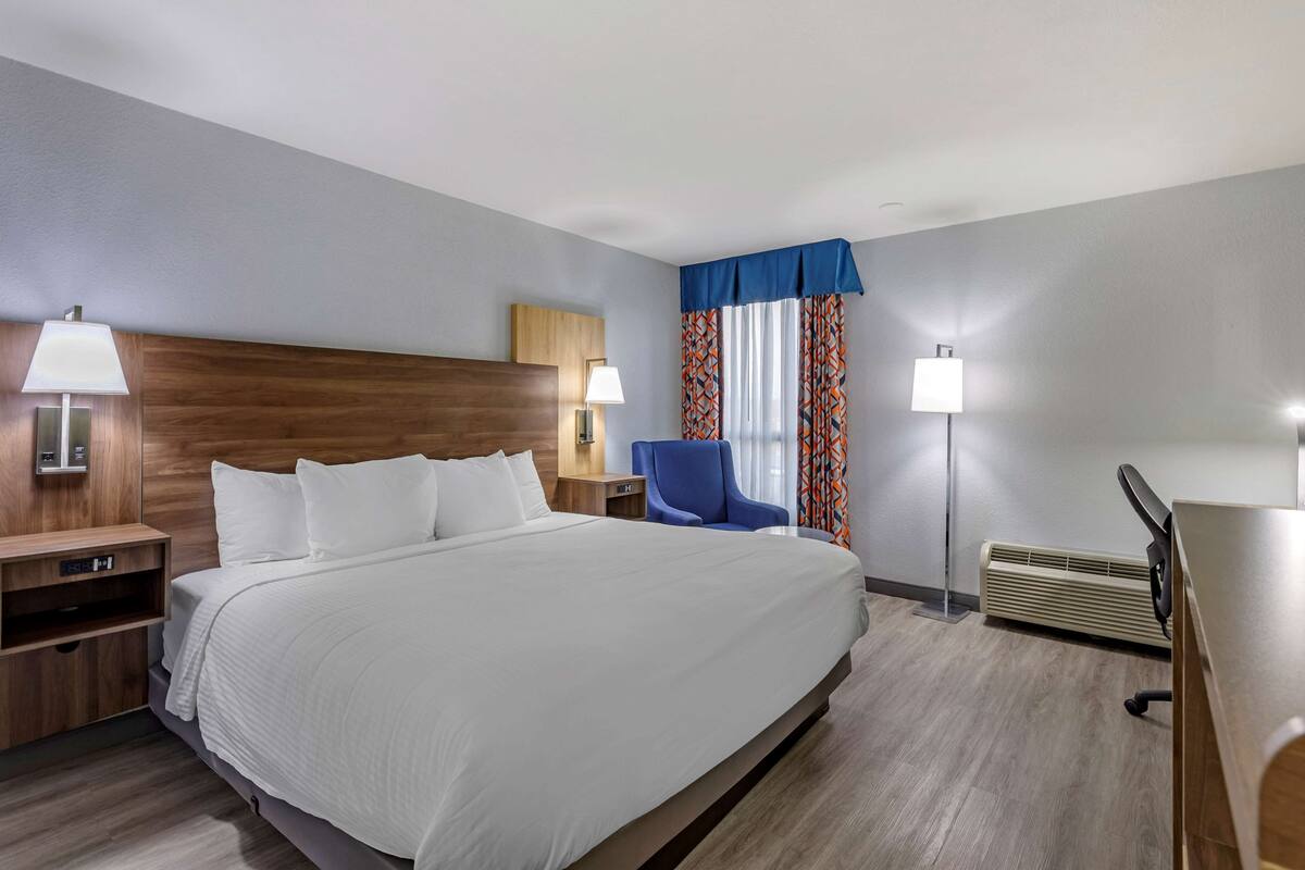 Een hotelkamer met een groot bed, nachtkastjes, een bureau, een stoel en een raam met gordijnen.