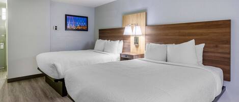 Una habitación de hotel con dos camas, una mesita de noche con lámpara, un cuadro enmarcado en la pared y un cabecero de madera.