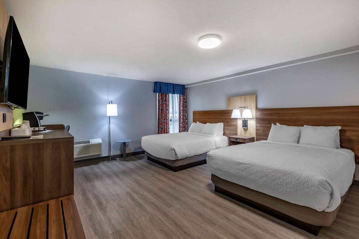 Een hotelkamer met twee bedden, een bureau, een televisie en een lamp.