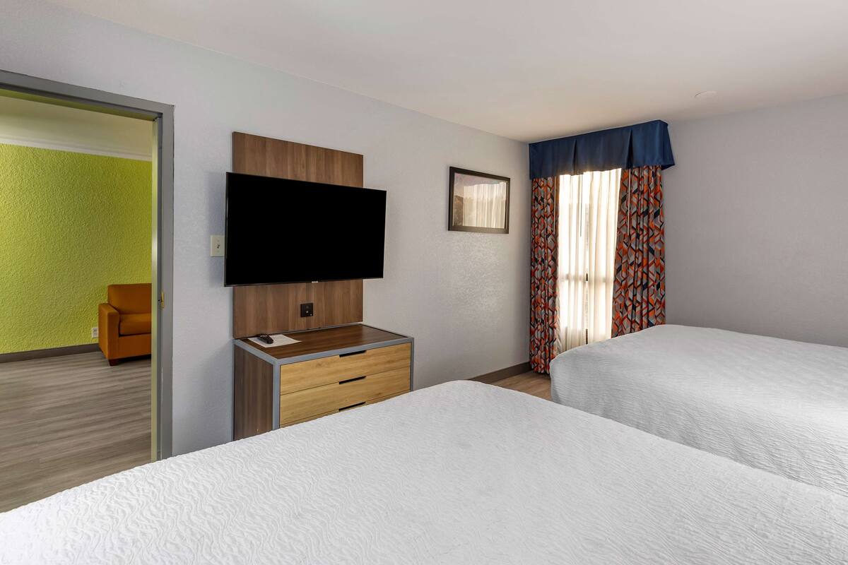 Een hotelkamer met twee bedden, een flatscreen televisie, een houten dressoir en een raam met gordijnen met een patroon.