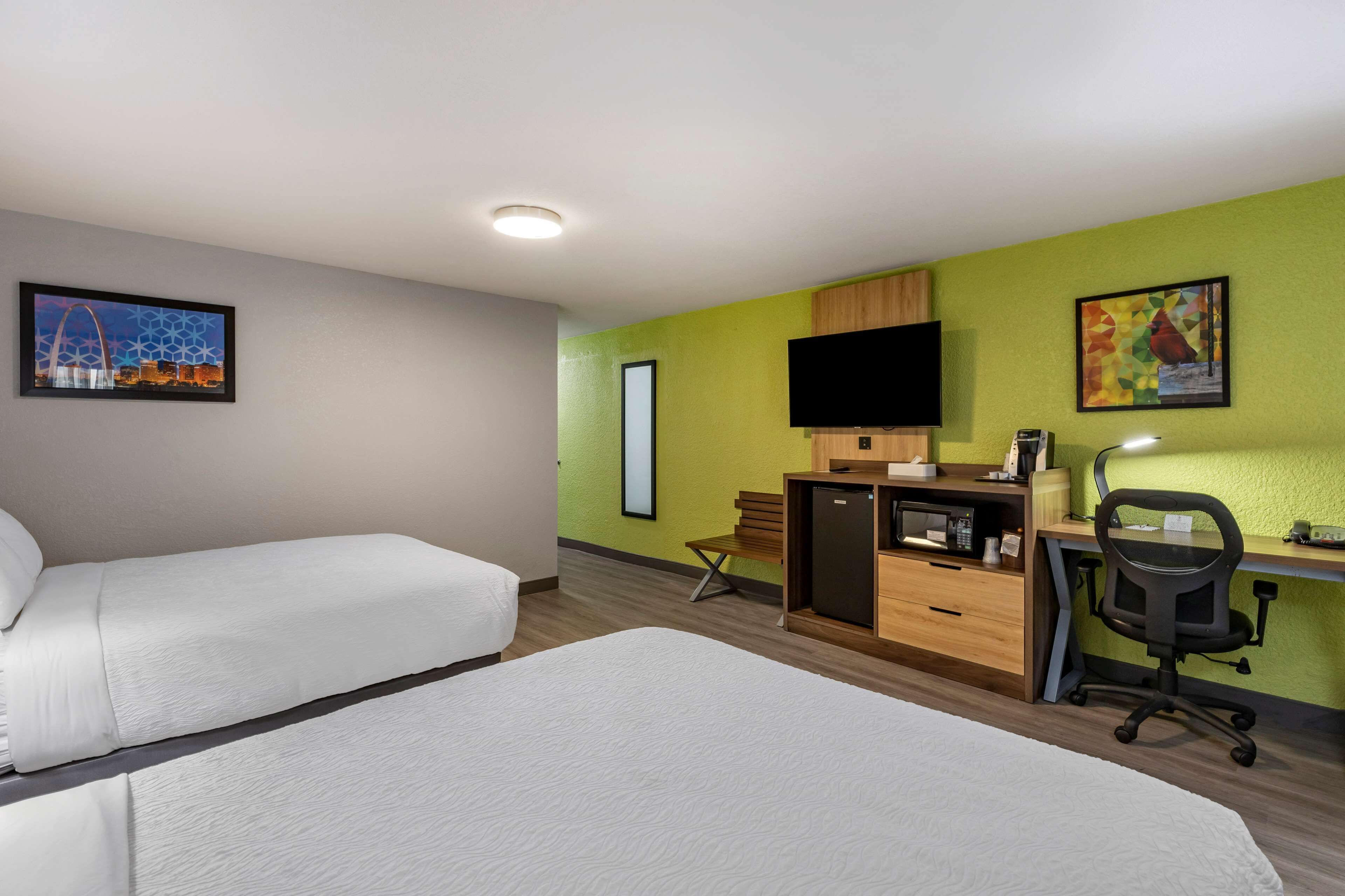 A hotel room with two beds, a desk with a computer, a chair, a TV, and artwork on the walls.