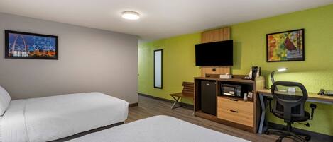 A hotel room with two beds, a desk with a computer, a chair, a TV, and artwork on the walls.