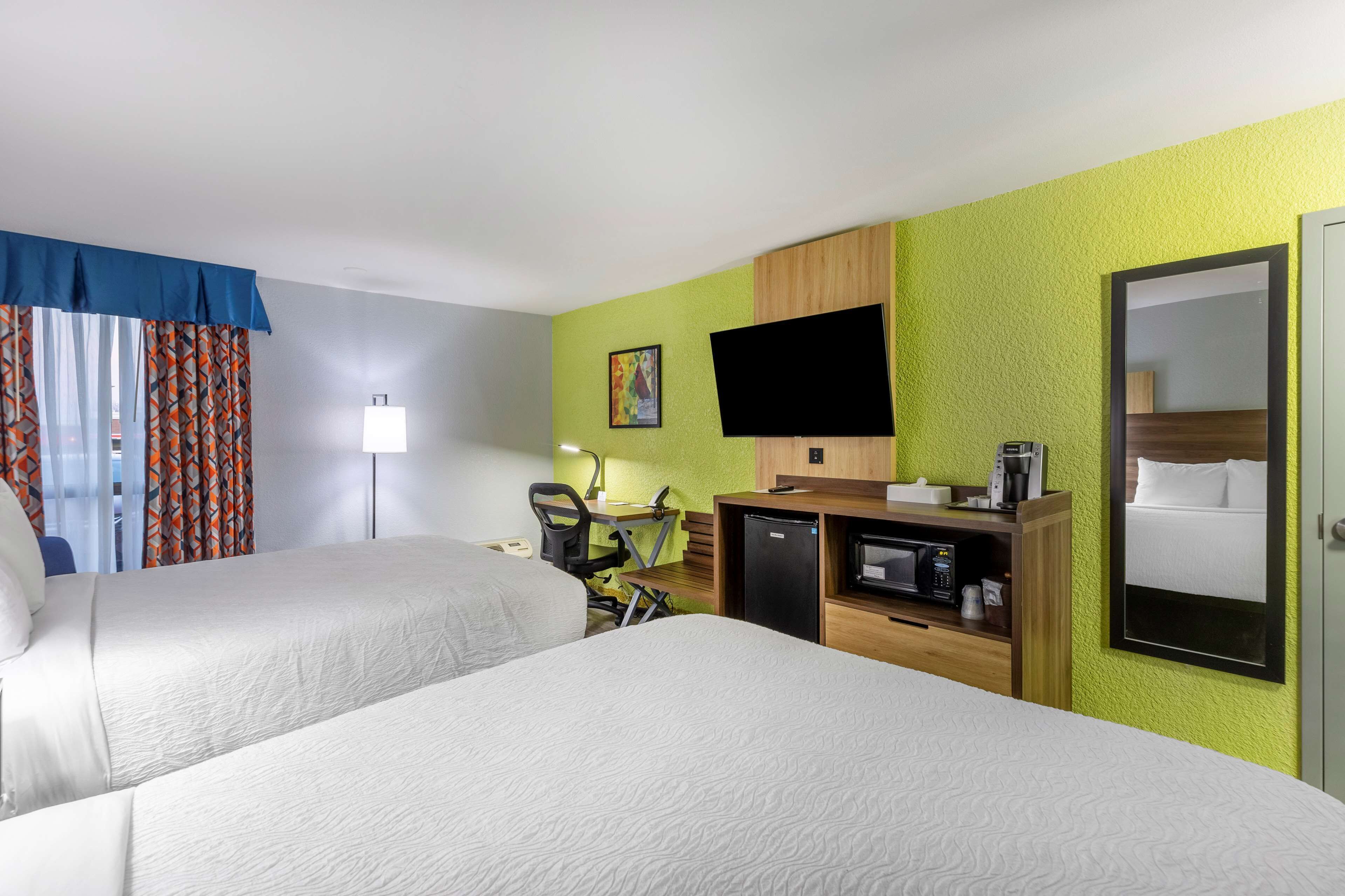Habitación de hotel con dos camas, un escritorio con silla, televisor, microondas y cafetera.