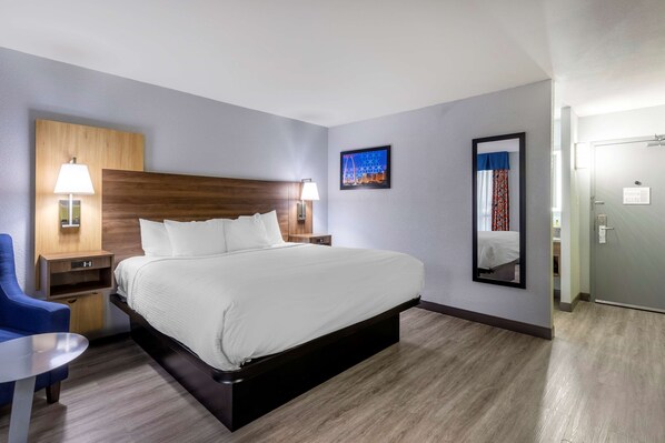 Habitación de hotel con una cama grande, mesitas de noche con lámparas, una silla azul y un espejo en la pared.