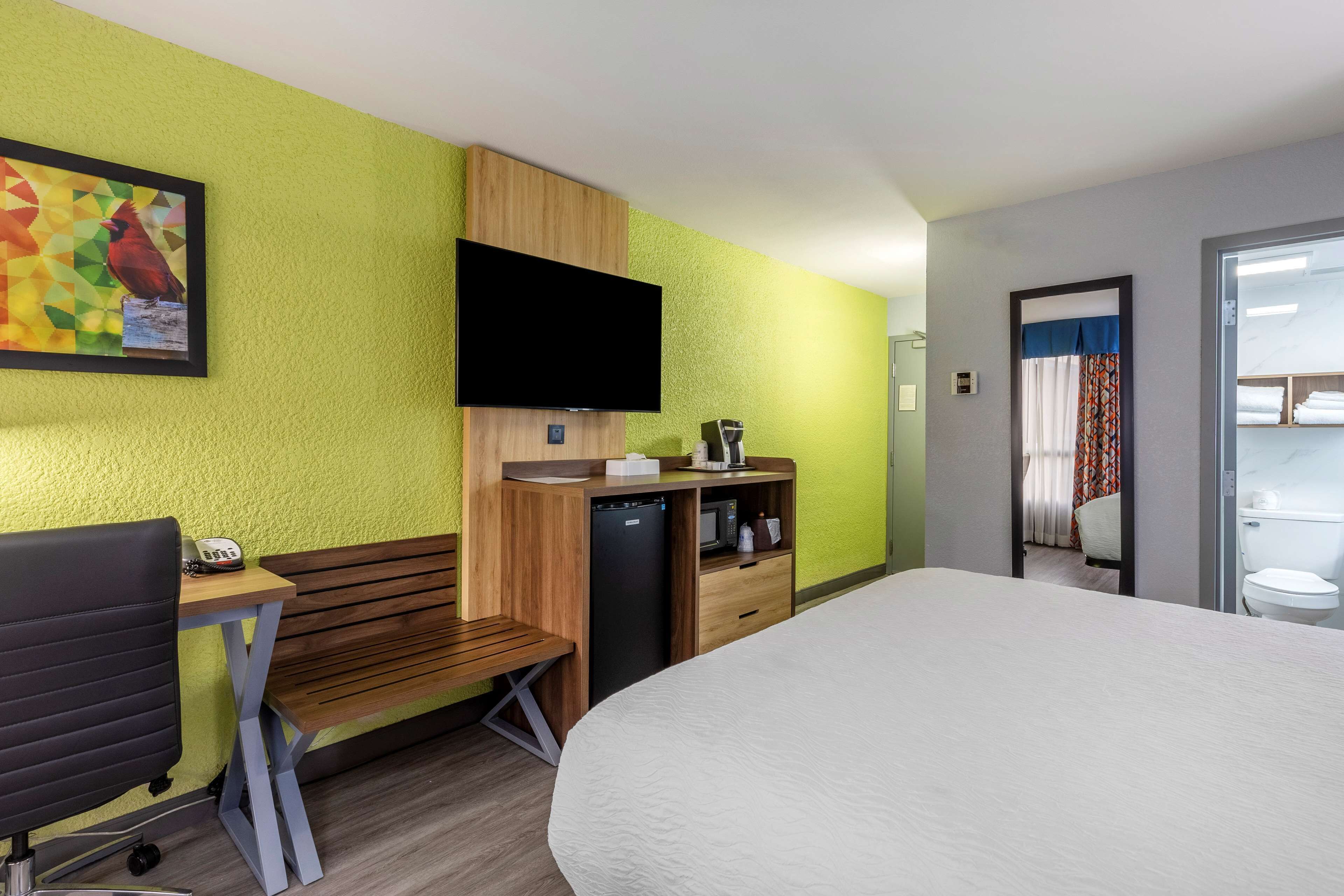 A hotel room with a bed, a desk with a chair, a television, and a small kitchenette.