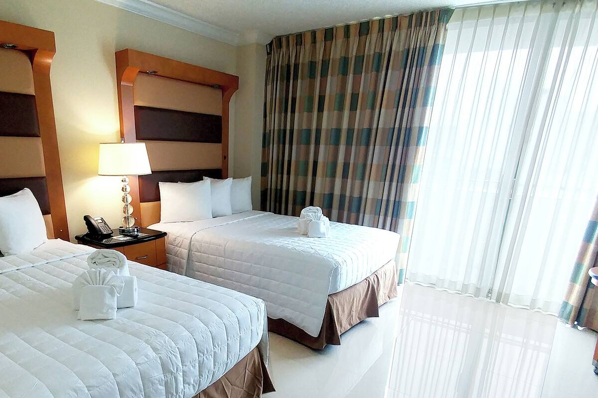 Une chambre d’hôtel avec deux lits, une table de chevet avec une lampe, un téléphone et une fenêtre avec des rideaux.