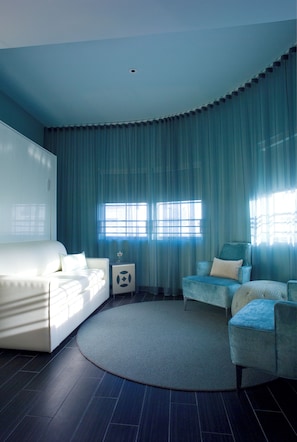 A modern hotel room with a curved ceiling, a white sofa, a blue armchair, and a round rug.
